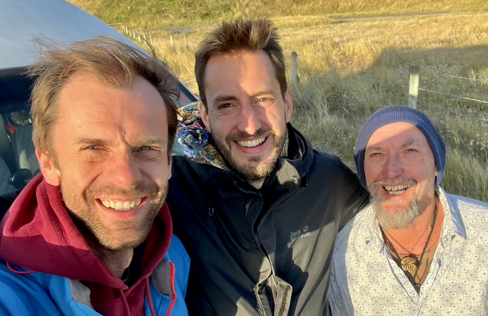 Three men standing together outdoors on a hillside